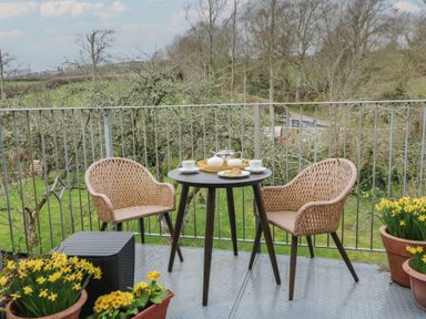 A balcony with two wicker chairs and a small table set for tea surrounded by potted flowers at Cantref House Top Floor in Brecon