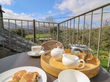 A balcony with a table set for tea including a teapot, cup, and plate of scones with countryside views at Cantref House Top Floor in Brecon