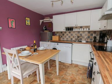 A kitchen with wooden table and chairs set for two with appliances and cabinets against purple walls at Cantref House Top Floor in Brecon