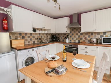 A kitchen with white cabinets wooden countertops a tiled backsplash and a wooden table set with plates bread and wine at Cantref House Top Floor in Brecon