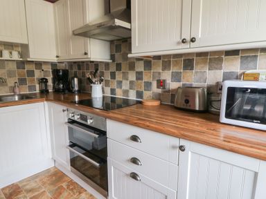 A kitchen with a wooden countertop white cabinets a stove oven toaster microwave and coffee maker at Cantref House Top Floor in Brecon