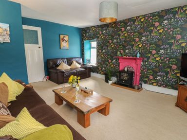 A living room with a brown sofa and a leather loveseat a wooden coffee table a floral wallpapered wall with a pink fireplace at Cantref House Top Floor in Brecon