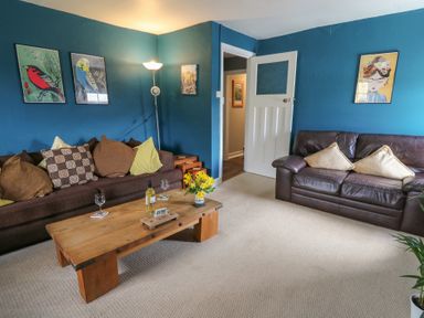 A living room with two sofas a wooden coffee table with wine glasses a bottle and flowers at Cantref House Top Floor in Brecon