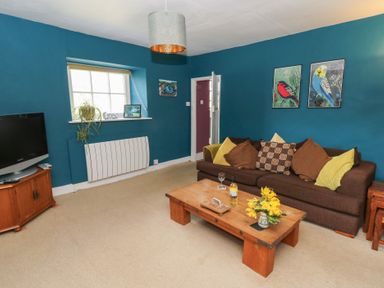 A living room with a brown sofa and wooden coffee table with flowers and wine bottle at Cantref House Top Floor in Brecon