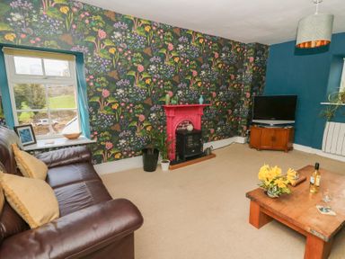 A living room with floral wallpaper a brown leather sofa a wooden coffee table a red fireplace and a television at Cantref House Top Floor in Brecon