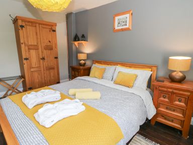 A bedroom with a double bed with yellow and gray bedding two nightstands with lamps a wooden wardrobe and framed artwork on the wall at Cantref House Top Floor in Brecon