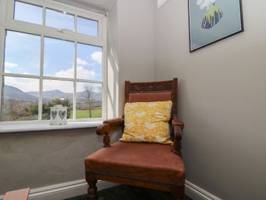 A wooden chair with leather seat and yellow cushion beside a window with view of hills and a white lantern on the windowsill at Cantref House Top Floor in Brecon