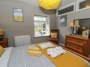 A bedroom with a bed with folded towels and robes a wooden dresser with a mirror and lamps a chair with a cushion and framed pictures on the walls at Cantref House Top Floor in Brecon