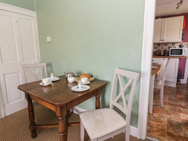 A dining area with a wooden table set for breakfast and two chairs next to a kitchen at Cantref House Top Floor in Brecon