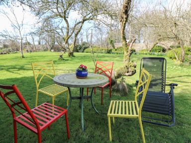 A round table with a plant in a pot surrounded by colorful chairs on grass in a garden at Cantref House Top Floor in Brecon