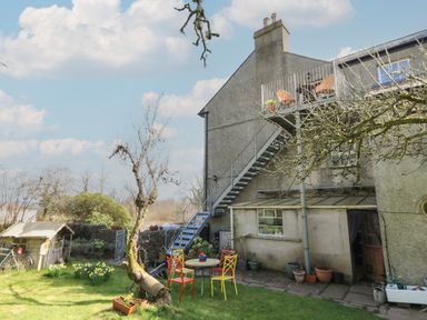 A garden with outdoor chairs and table near a house with stairs leading to a balcony at Cantref House Top Floor in Brecon