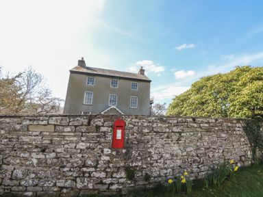 A stone wall with a red post box and yellow flowers in front of a large house and shrubbery at Cantref House Top Floor in Brecon
