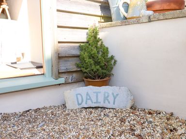 A small potted plant and a concrete sign with the word dairy on gravel outside a light-colored building at The Dairy at Wyke Farm Wyke near Lyme Regis