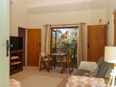 A sitting room with a small wooden table and chairs a TV and sofa open doors showing a horse outside at The Dairy at Wyke Farm  Wyke near Lyme Regis