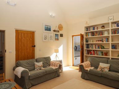 A living room with two sofas a lamp a bookshelf and an open door at The Dairy at Wyke Farm Wyke near Lyme Regis