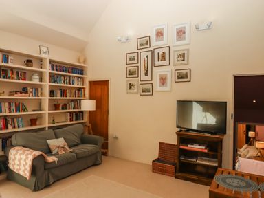 A living room with a green sofa and bookshelf a wooden TV stand and framed pictures on the wall at The Dairy at Wyke Farm Wyke near Lyme Regis