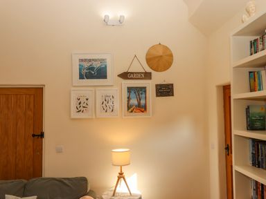 A wall with framed pictures a garden sign lamp on a table sofa wooden doors and a bookshelf at The Dairy at Wyke Farm in Wyke near Lyme Regis