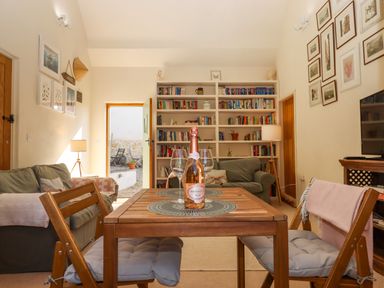 A dining table with a bottle and glasses surrounded by chairs in a living room with sofas bookshelves and framed pictures at The Dairy at Wyke Farm Wyke near Lyme Regis