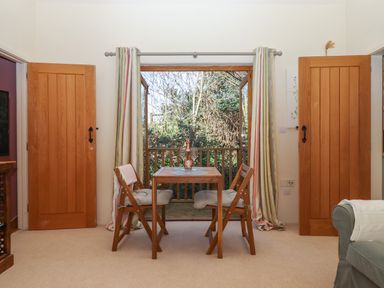 A dining area with a wooden table and two chairs near an open door leading to a balcony at The Dairy at Wyke Farm Wyke near Lyme Regis