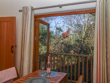 A wooden table with two wine glasses and a bottle next to an open door showing a balcony and trees outside at The Dairy at Wyke Farm Wyke near Lyme Regis