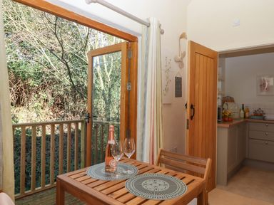 A wooden table with two wine glasses and a bottle of prosecco next to an open door leading to a balcony and a kitchen at The Dairy at Wyke Farm Wyke near Lyme Regis
