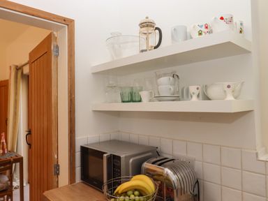 A kitchen corner with wooden door microwave toaster fruit basket and shelves with cups and glassware at The Dairy at Wyke Farm Wyke near Lyme Regis