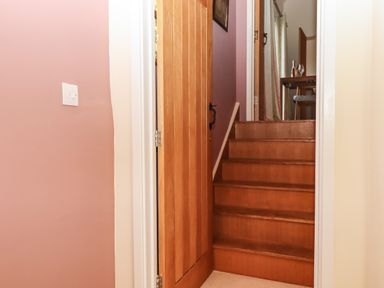 Wooden stairs leading up with an open wooden door and a light switch on a pink wall at The Dairy at Wyke Farm in Wyke near Lyme Regis