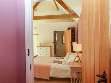 A bedroom with a double bed bedside tables with lamps a dresser and an open door leading to a bathroom at The Dairy at Wyke Farm Wyke near Lyme Regis