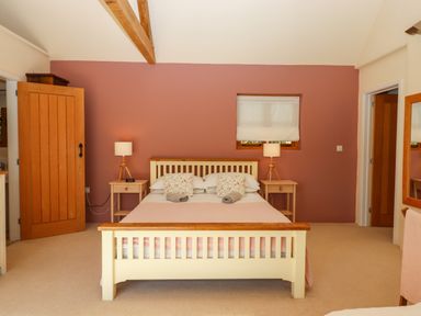 A bedroom with a bed, two bedside tables with lamps, an open door, window with blind, and a mirror at The Dairy at Wyke Farm Wyke near Lyme Regis