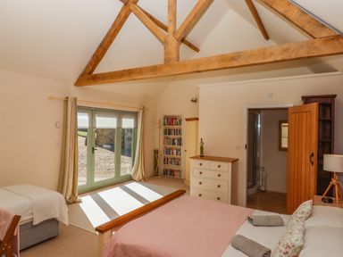 A bedroom with exposed wooden beams double and single beds dresser bookshelf and glass doors at The Dairy at Wyke Farm Wyke near Lyme Regis