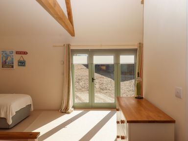 A bedroom with a bed, a wooden dresser, glass doors with curtains, and wall decorations at The Dairy at Wyke Farm in Wyke near Lyme Regis