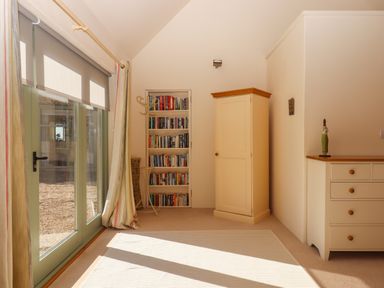 A room with glass doors, a small bookcase, a corner wardrobe, and a chest of drawers at The Dairy at Wyke Farm in Wyke near Lyme Regis