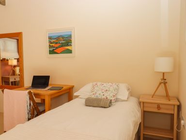 A bedroom with a single bed a pillow and towel a wooden desk with a laptop and a chair with a blanket a bedside table with a lamp at The Dairy at Wyke Farm in Wyke near Lyme Regis