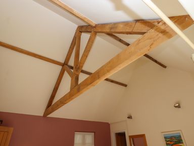 A ceiling with wooden beams in a room with a maroon wall and a framed picture at The Dairy at Wyke Farm Wyke near Lyme Regis