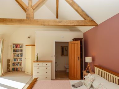 A bedroom with wooden beams a bed a chest of drawers an open door showing a bathroom and a bookshelf at The Dairy at Wyke Farm in Wyke near Lyme Regis