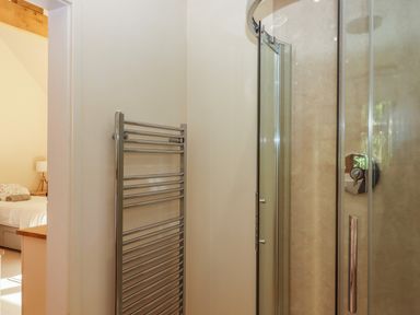A bathroom with a glass shower door and a metal towel radiator near a bedroom at The Dairy at Wyke Farm Wyke near Lyme Regis