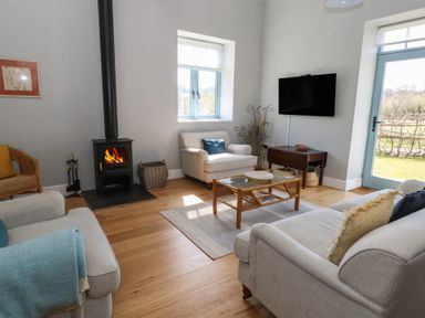 A living room with two beige sofas a wicker chair a wood burning stove a wall mounted tv and a blue door at Stapleford Farm in Hooke near Beaminster