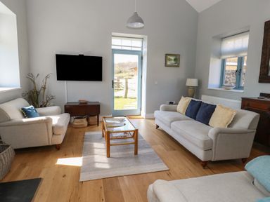 A living room with two sofas a coffee table a wall-mounted tv and a door leading outside at Stapleford Farm Hooke near Beaminster