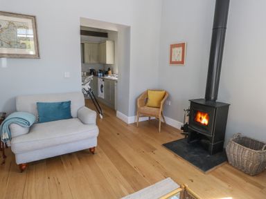 A living room with a wood stove a grey sofa with blue pillow a wicker chair with yellow pillow and an open doorway to a kitchen at Stapleford Farm in Hooke near Beaminster