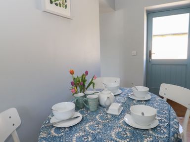 A dining area with a round table set with white bowls, cups, a teapot, a butter dish, and a vase of tulips at Stapleford Farm in Hooke near Beaminster