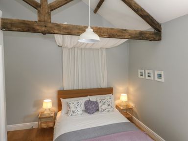 A bedroom with a bed with floral pillows and a purple heart pillow two bedside tables with lamps and wooden ceiling beams at Stapleford Farm in Hooke near Beaminster