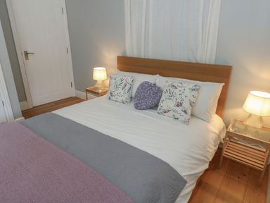 A bedroom with a double bed with floral and heart-shaped cushions bedside tables with lamps and a wooden floor at Stapleford Farm in Hooke near Beaminster