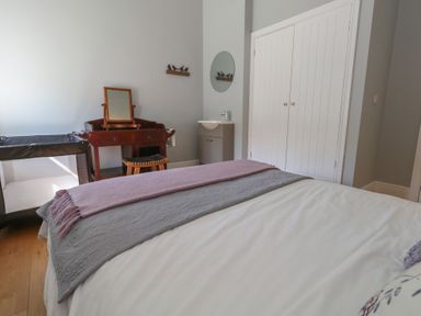 A bedroom with a bed, a wooden vanity table with a mirror, a changing stool, a baby crib, a small sink with a round mirror and white double doors at Stapleford Farm in Hooke near Beaminster