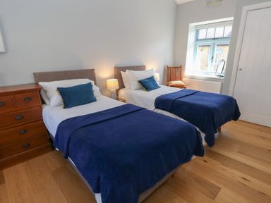 A bedroom with two single beds with blue blankets and pillows a wooden chest of drawers a wooden chair and a window at Stapleford Farm Hooke near Beaminster