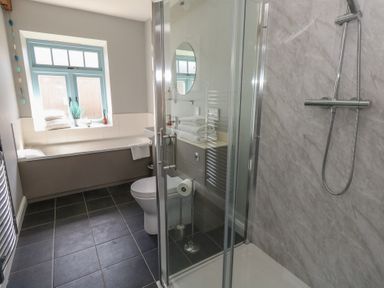 A bathroom with a bathtub a toilet a shower with glass doors and a window at Stapleford Farm in Hooke near Beaminster