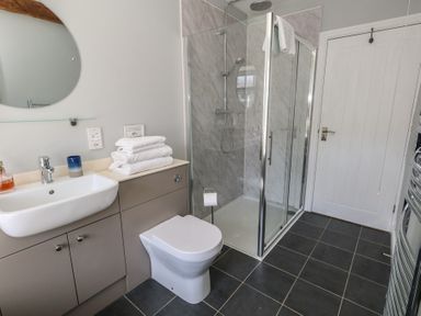 A bathroom with a shower enclosure a toilet a sink with towels on the countertop and a circular mirror on the wall at Stapleford Farm in Hooke near Beaminster