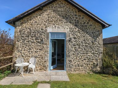 A stone building exterior with a blue door and white metal table and chairs on a stone patio at Stapleford Farm in Hooke near Beaminster
