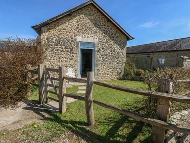 A stone building with an open blue door and a wooden gate with fence around a small grass garden at Stapleford Farm in Hooke near Beaminster