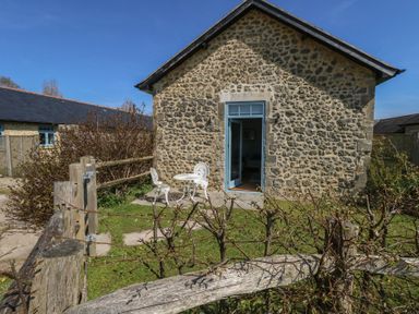 A stone building with an open blue door and white metal table and chairs outside at Stapleford Farm Hooke near Beaminster