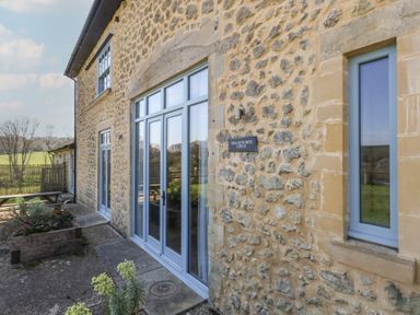 Exterior of a stone building with blue framed windows and doors and a garden area at Stapleford Farm in Hooke near Beaminster
